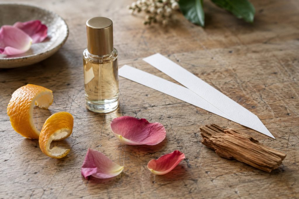Citrus peel, rose petals, wood and perfume blotters beside a generic vial